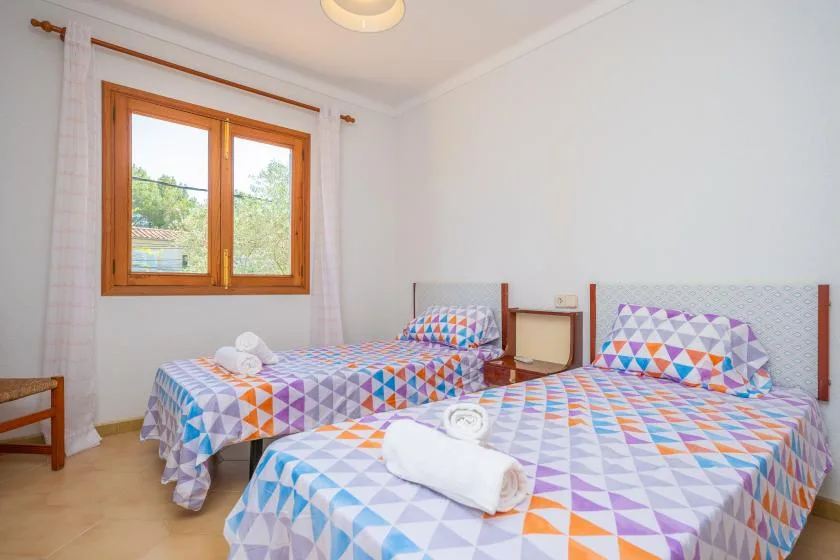 A bright bedroom with two beds dressed in colorful geometric-patterned bedding.