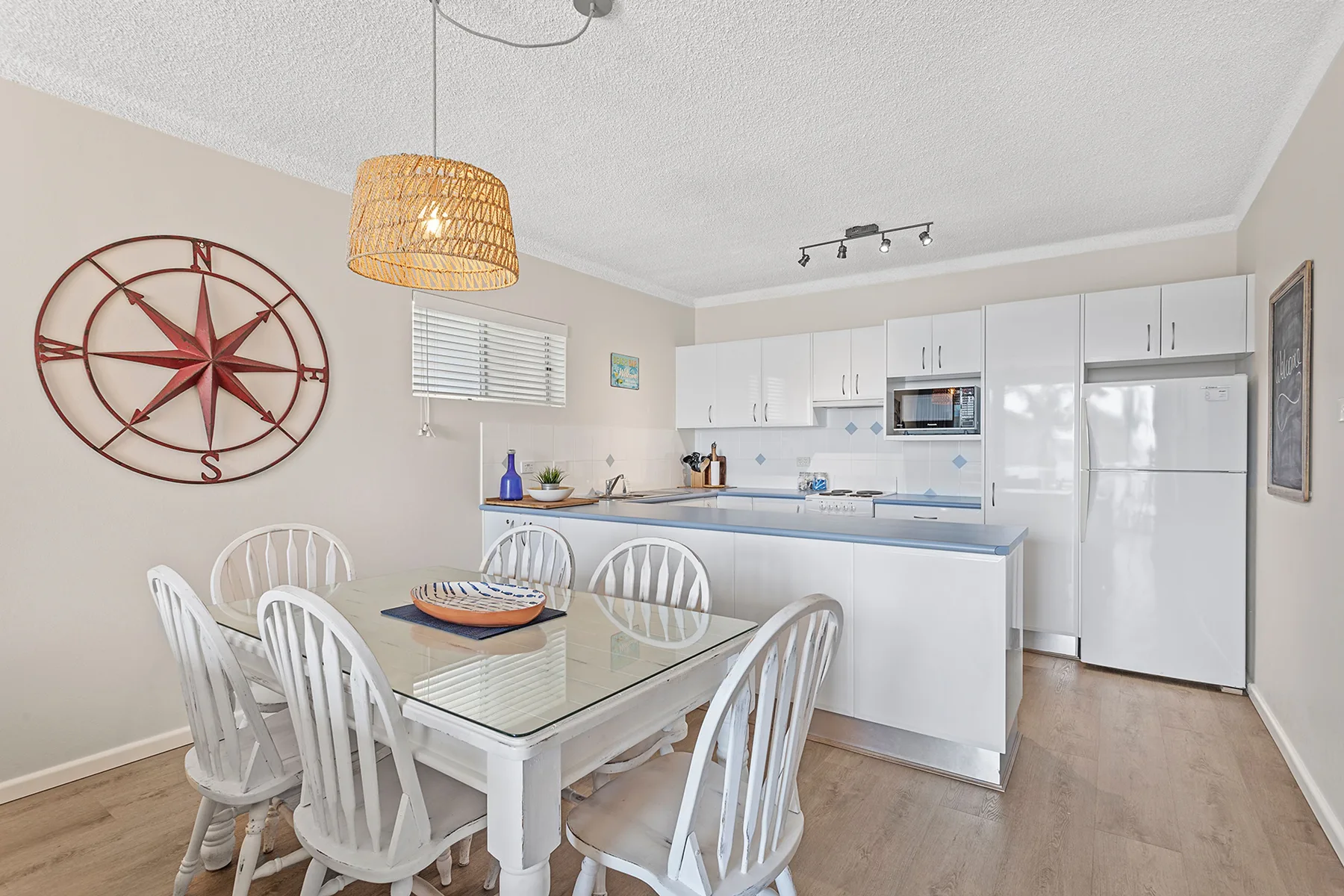 A dining area with a glass table beside a bright kitchen.