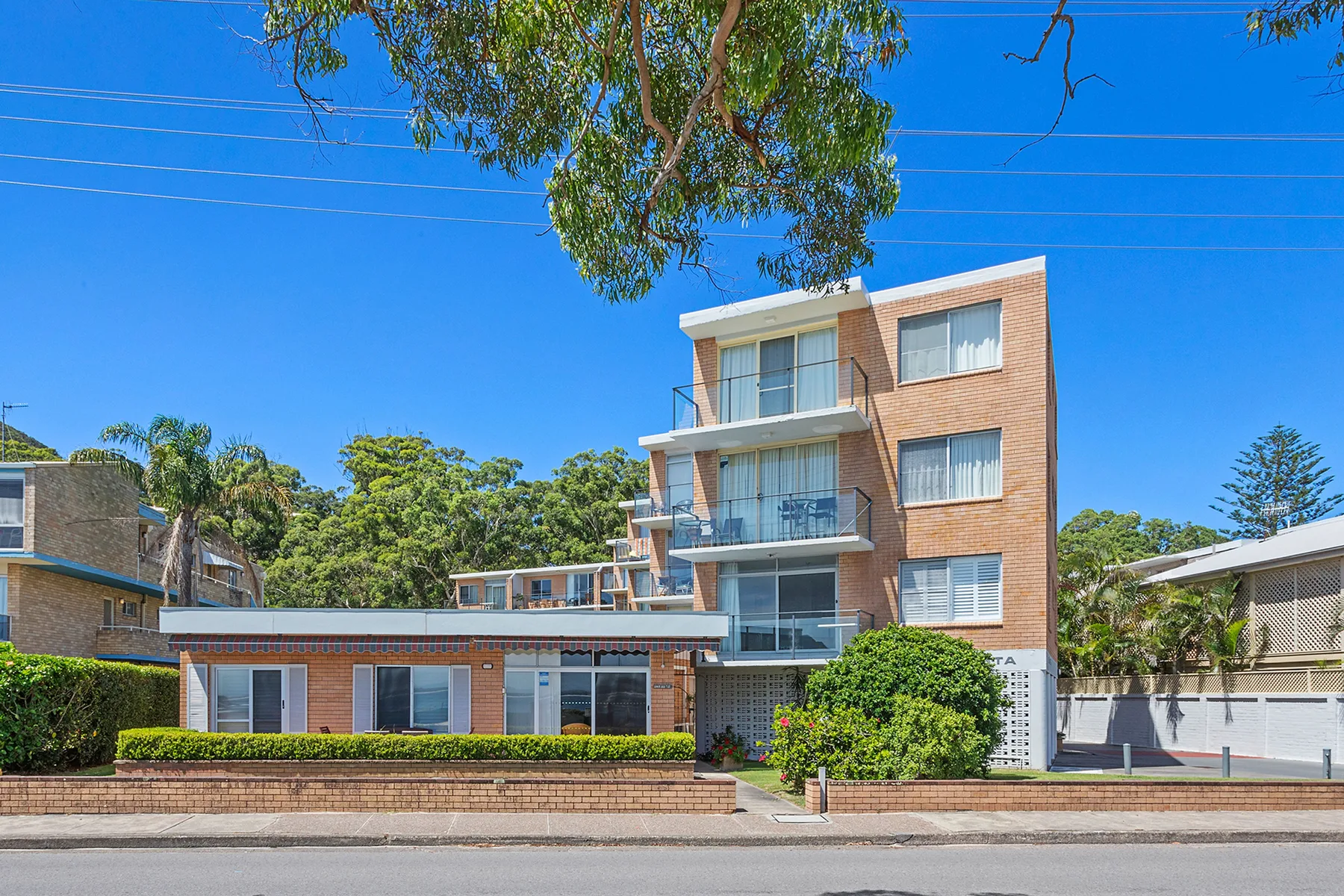 A multi-story brick apartment building stands beside landscaped greenery.