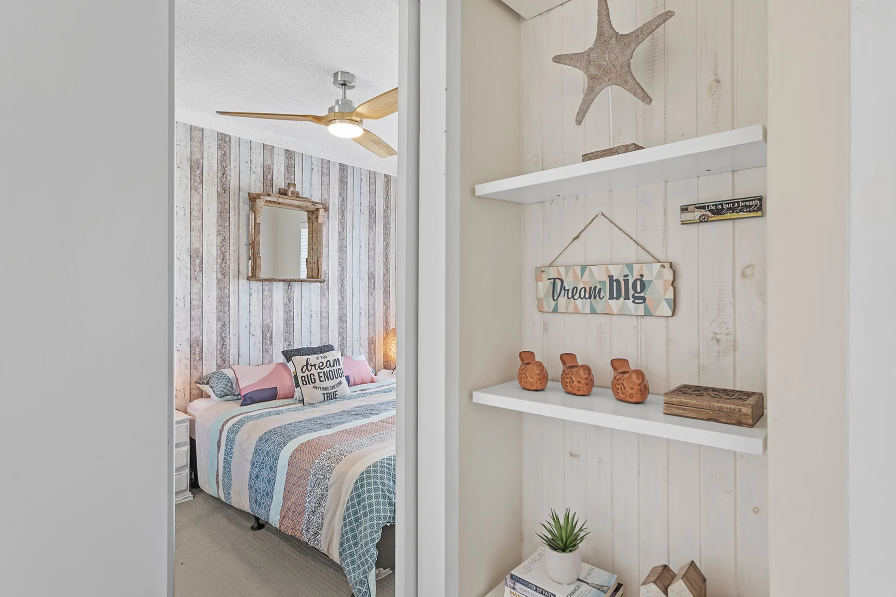 A bedroom is visible through a doorway beside wall shelves with coastal decorations.