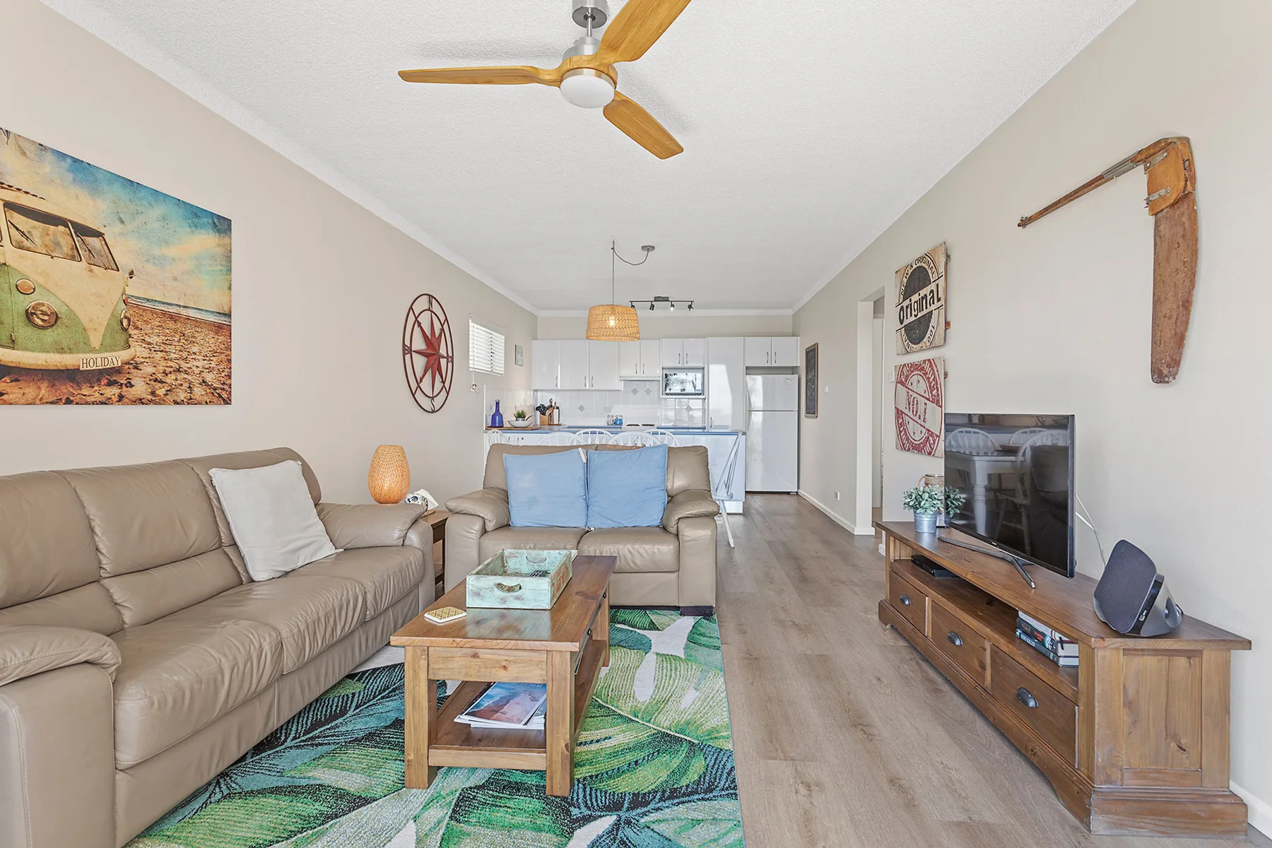 A living room with seating, a television, and an open kitchen in the background.