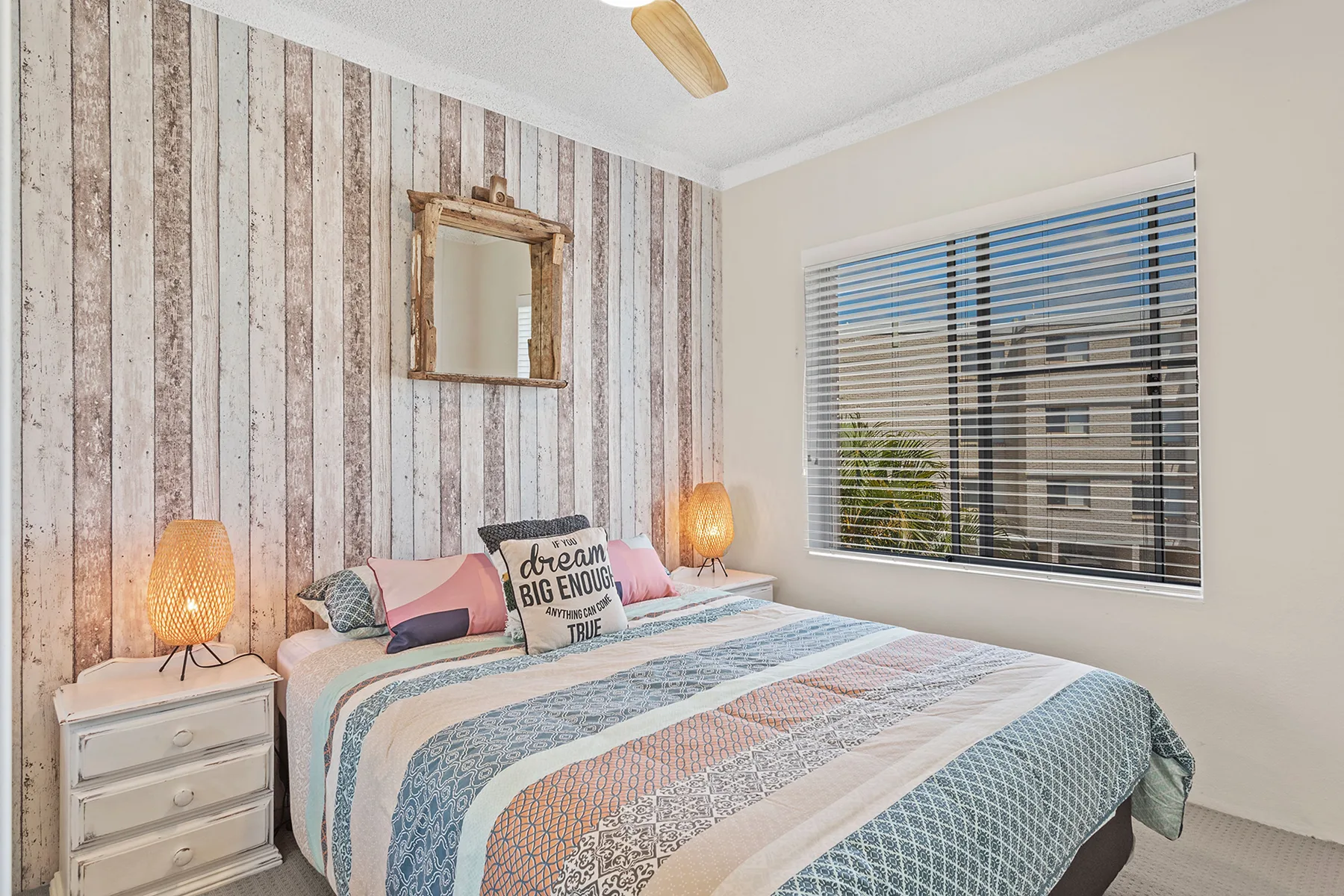 A bedroom with a patterned bedspread, bedside tables, and a window with blinds.