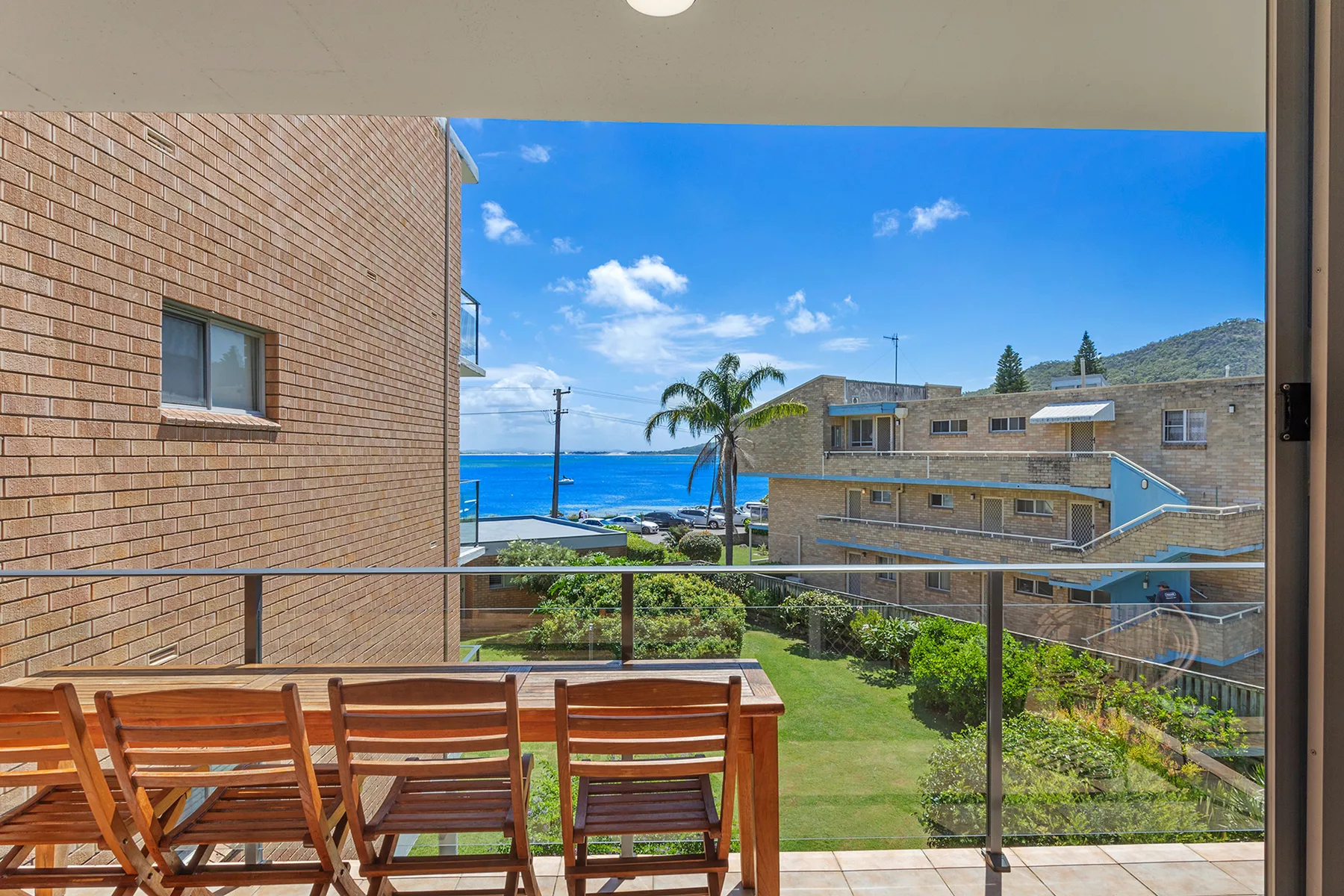A balcony with outdoor seating overlooks nearby buildings and a glimpse of the sea.
