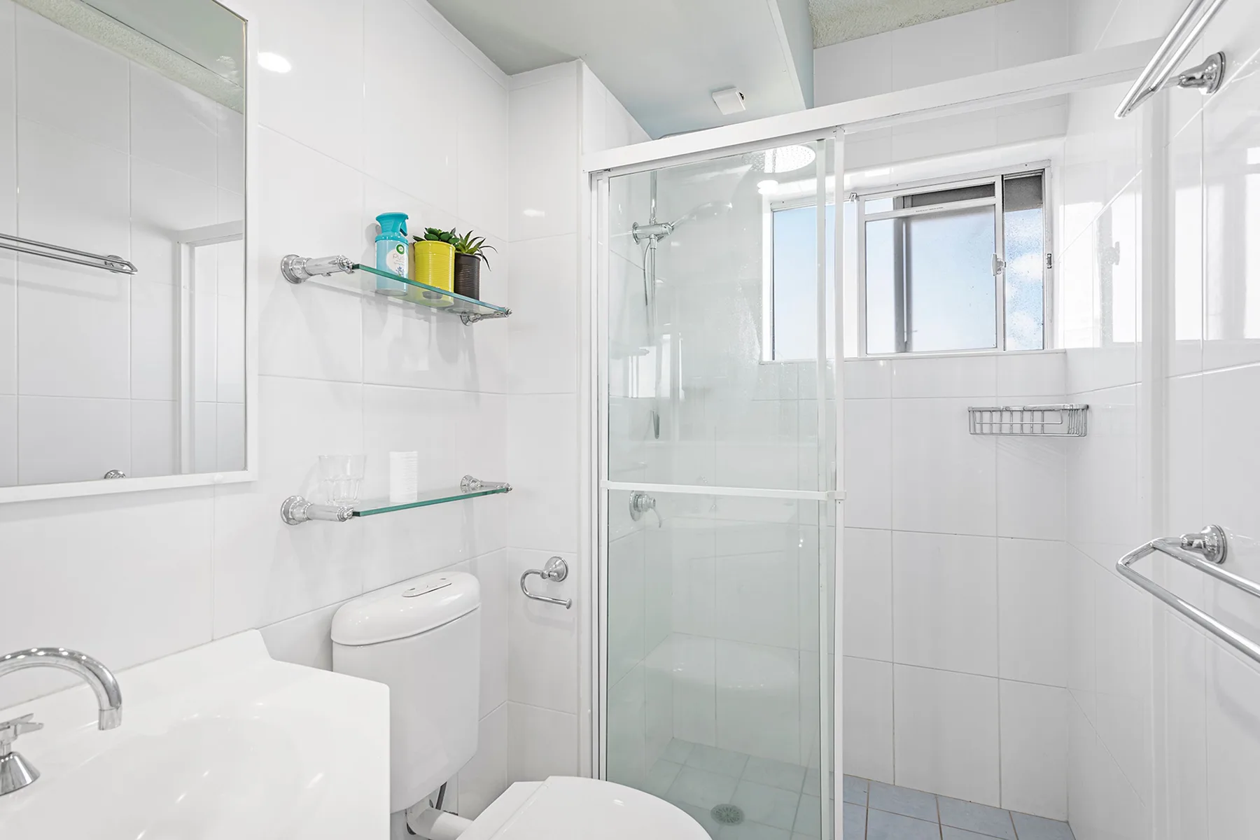 A bright tiled bathroom with a sink, toilet, and glass shower.