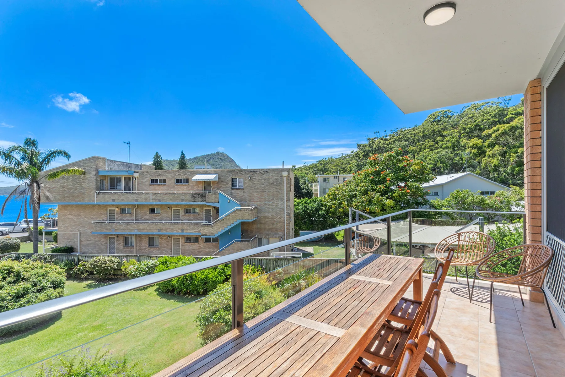 A balcony with wooden seating overlooks landscaped grounds and nearby buildings.