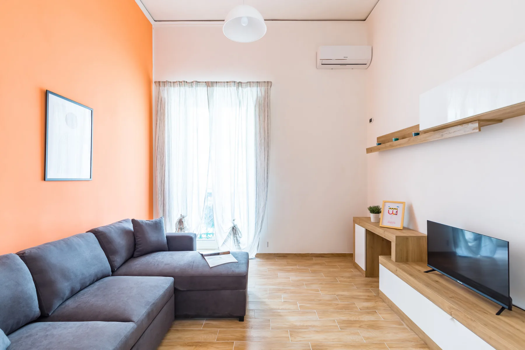 A living room with a sectional sofa, a television, and a bright curtained window.