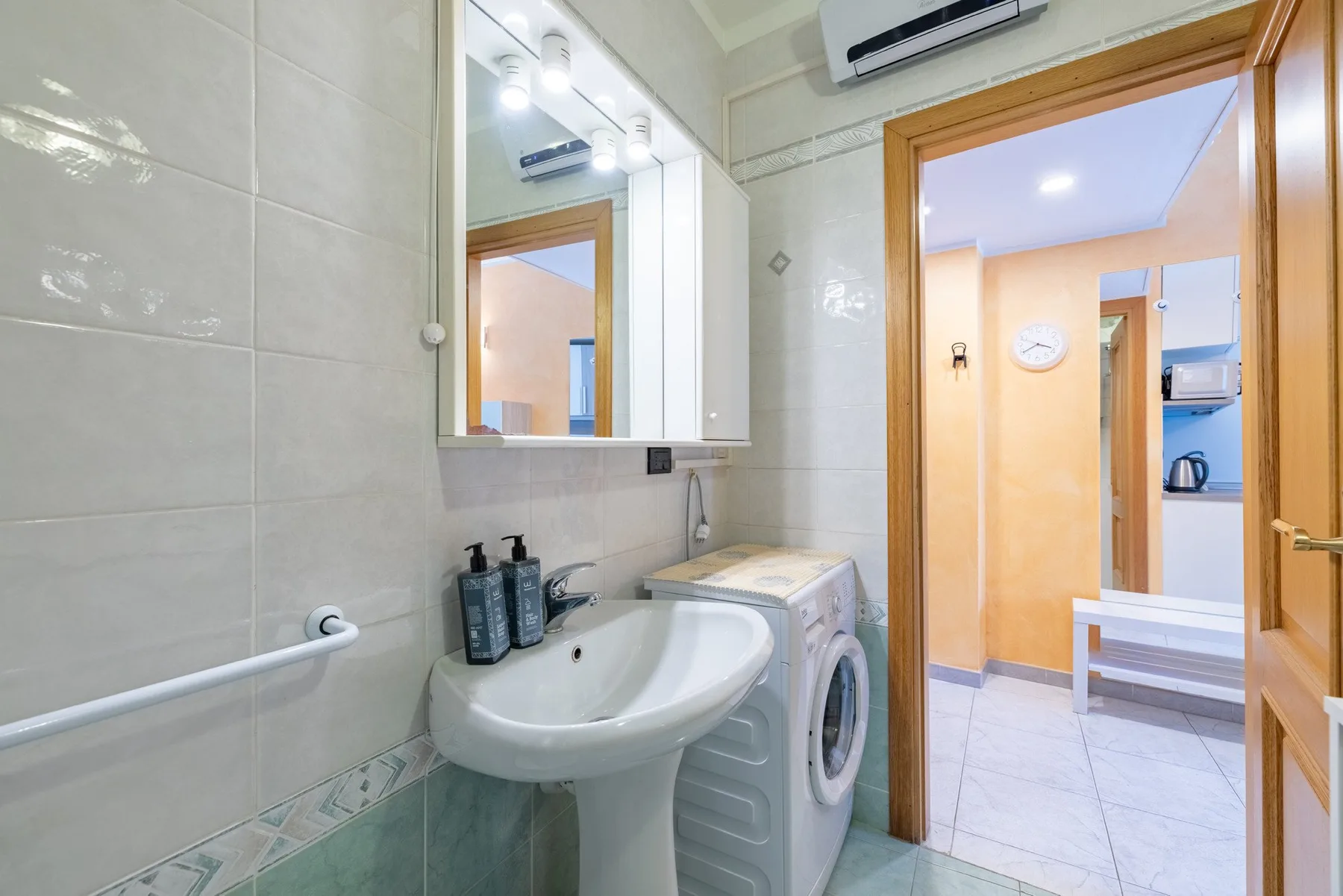 Un baño alicatado con lavabo, espejo y lavadora.