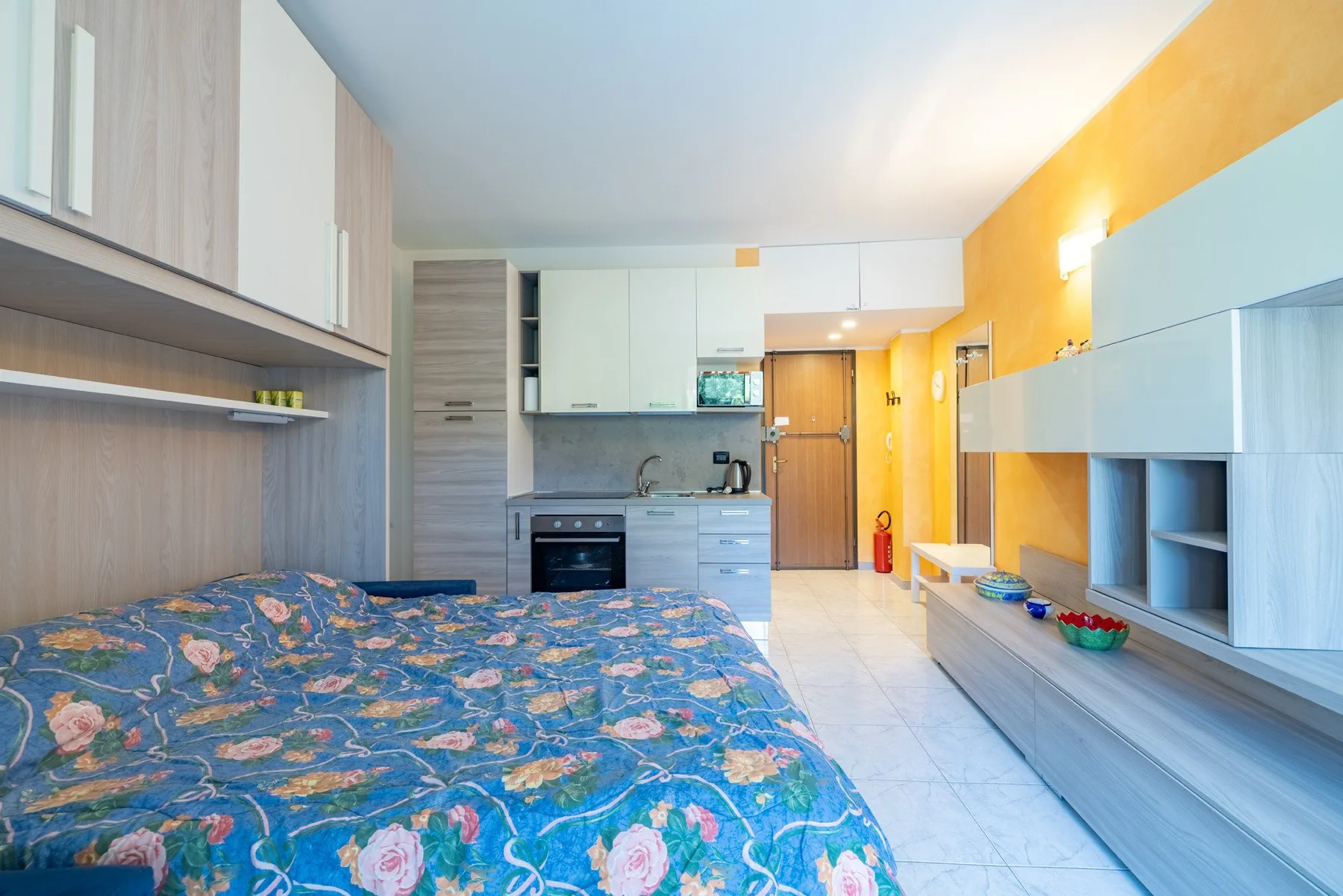 Dormitorio con una colcha estampada, armarios empotrados y una pequeña cocina.
