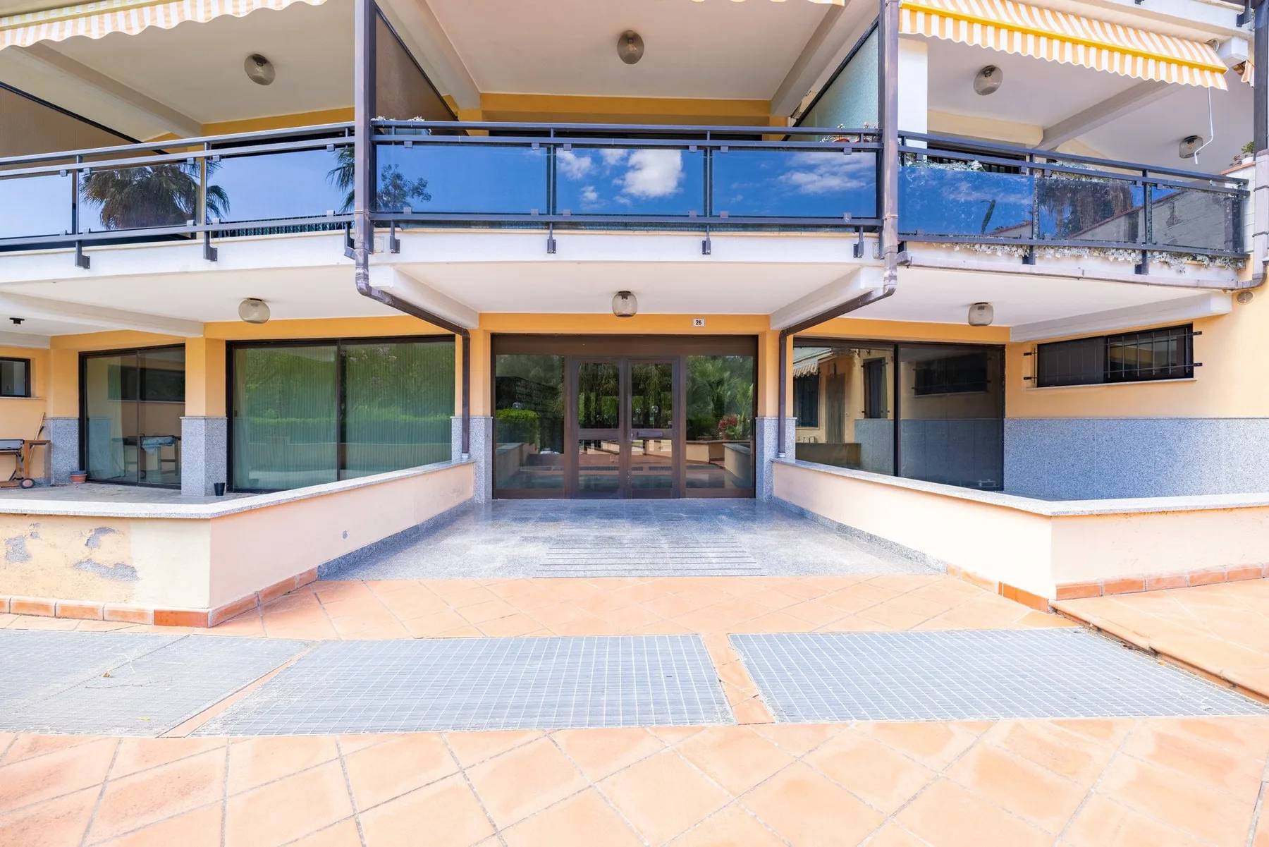 La entrada del edificio da a un patio pavimentado, con balcones de vidrio arriba.