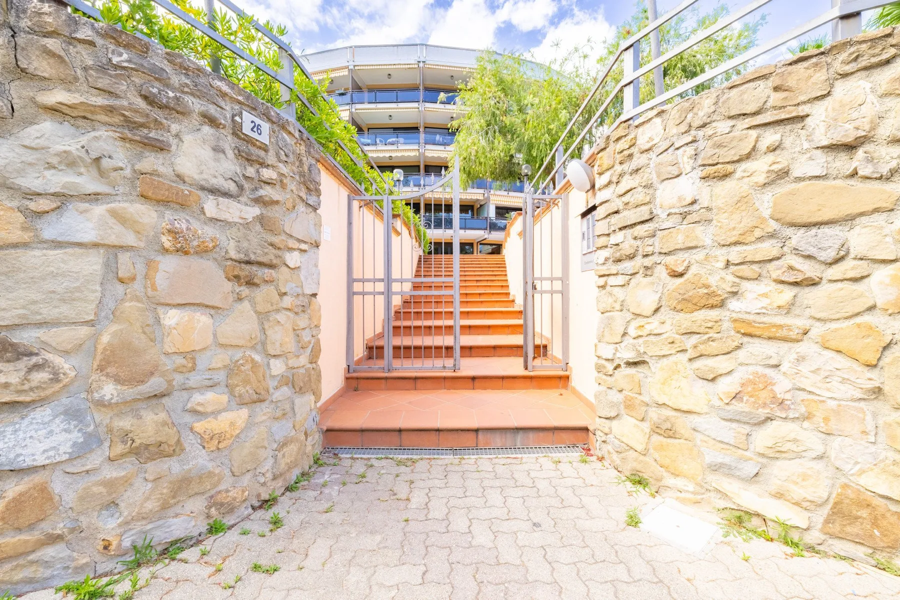 Una entrada exterior con muros de piedra conduce a una escalera entre barandillas metálicas.