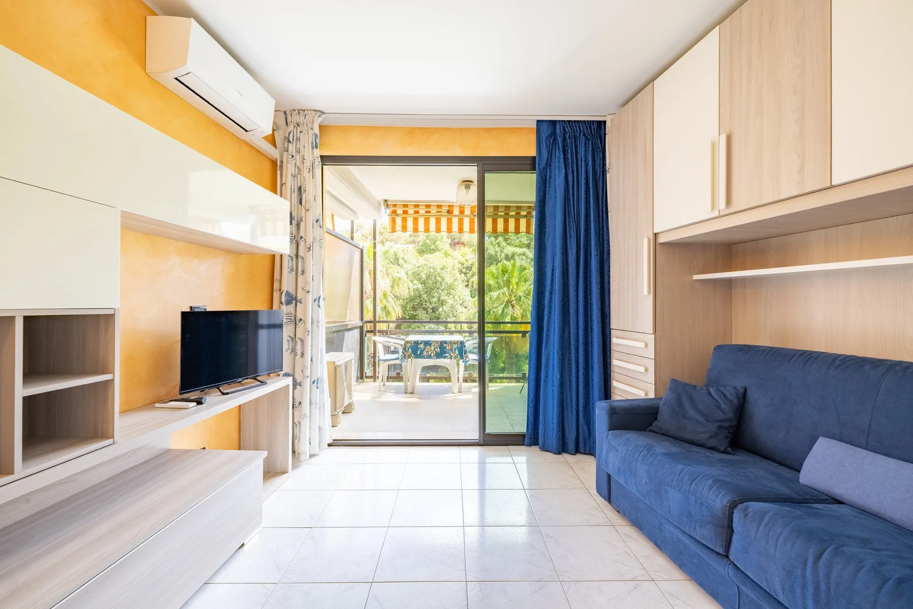 Una sala luminosa con asientos azules y puertas de vidrio que dan a un balcón.