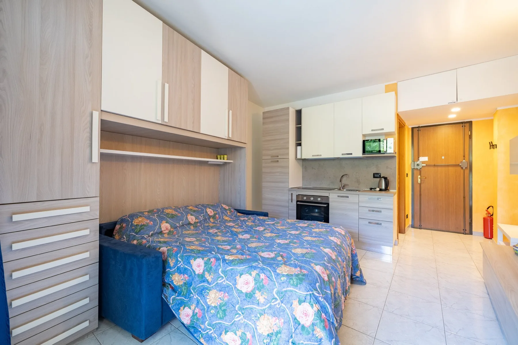 Un dormitorio con una colcha estampada junto a una pequeña cocina.