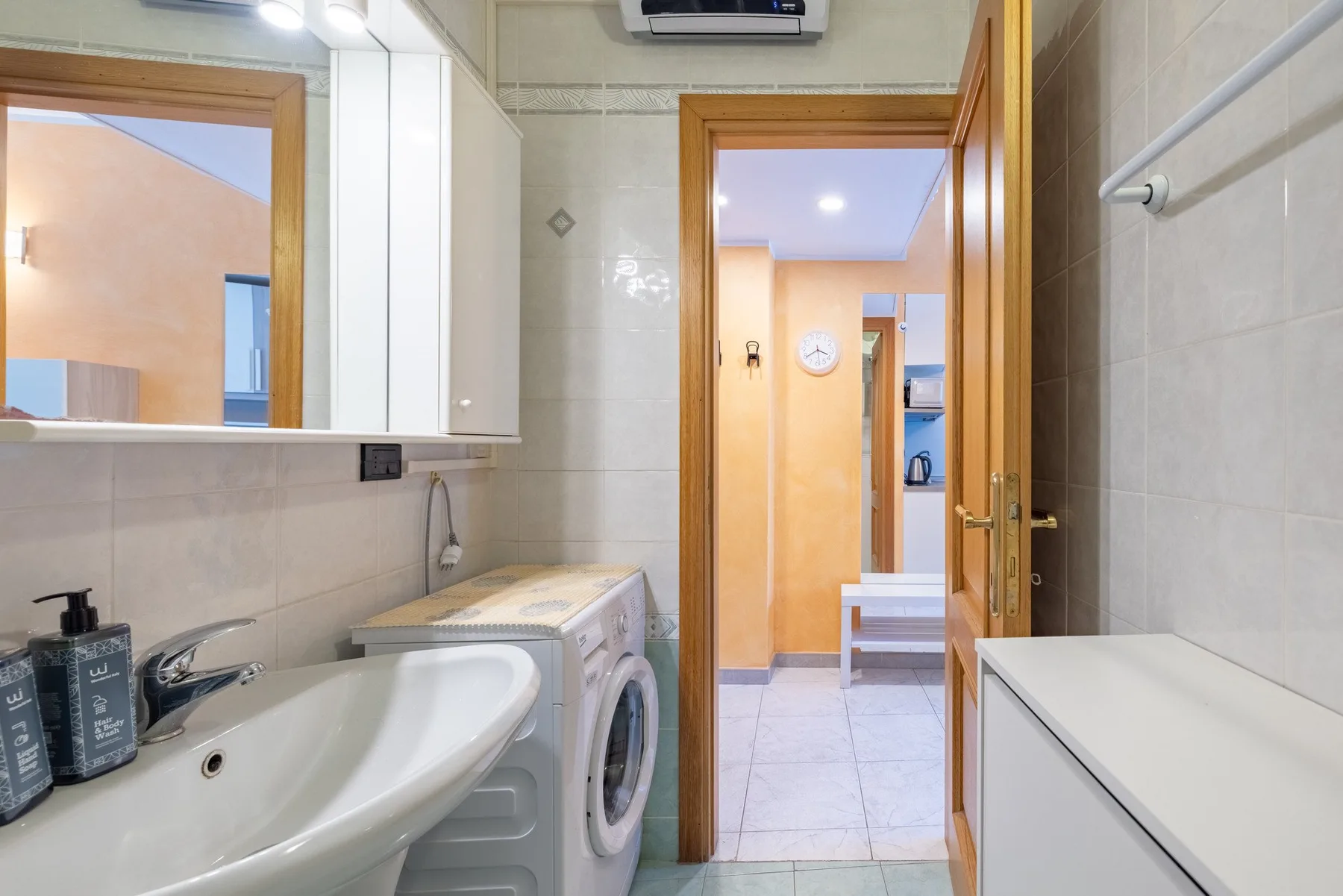 Un baño alicatado con lavabo, lavadora y una puerta abierta.