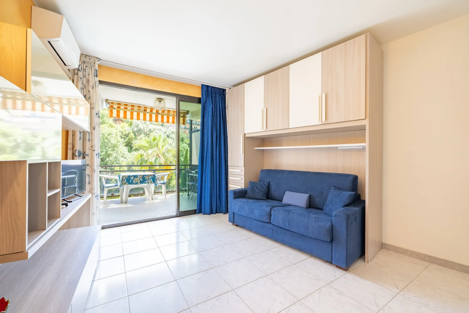 Una sala luminosa con asientos azules y una puerta de vidrio que da a un balcón.