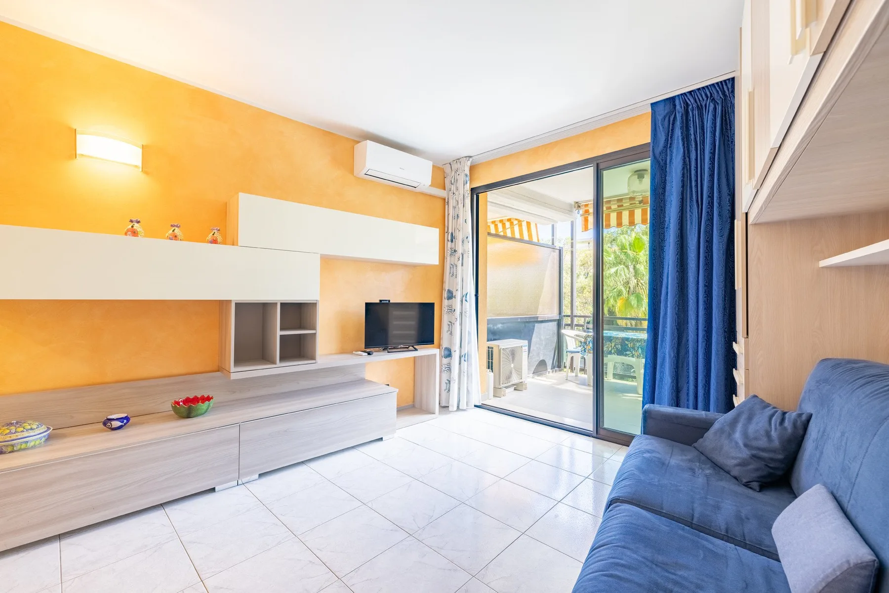 Una sala luminosa con asientos azules y puertas corredizas de vidrio hacia un balcón.