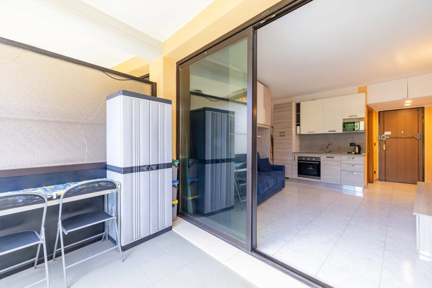 Un patio de baldosas se abre a una cocina compacta y una sala mediante puertas corredizas de vidrio.