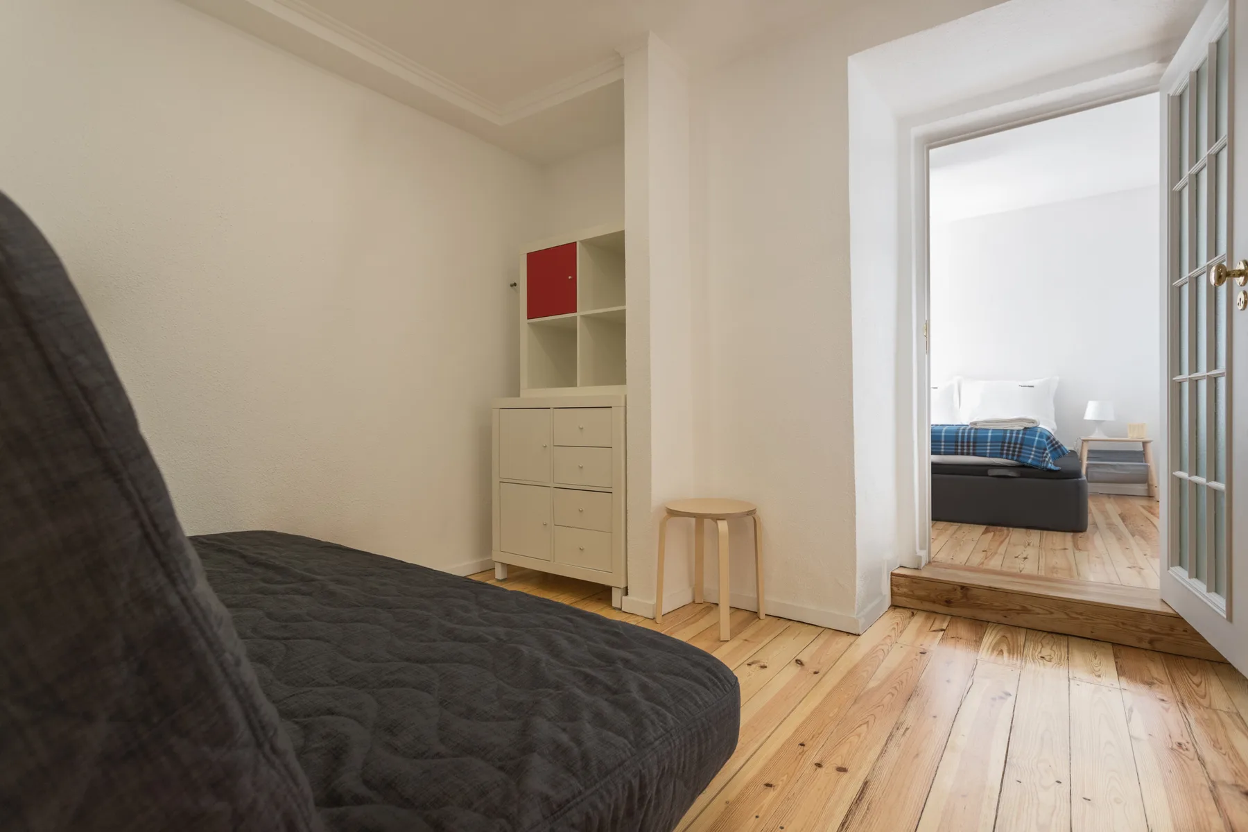 Un dormitorio luminoso con una cama oscura, suelo de madera y una puerta abierta.