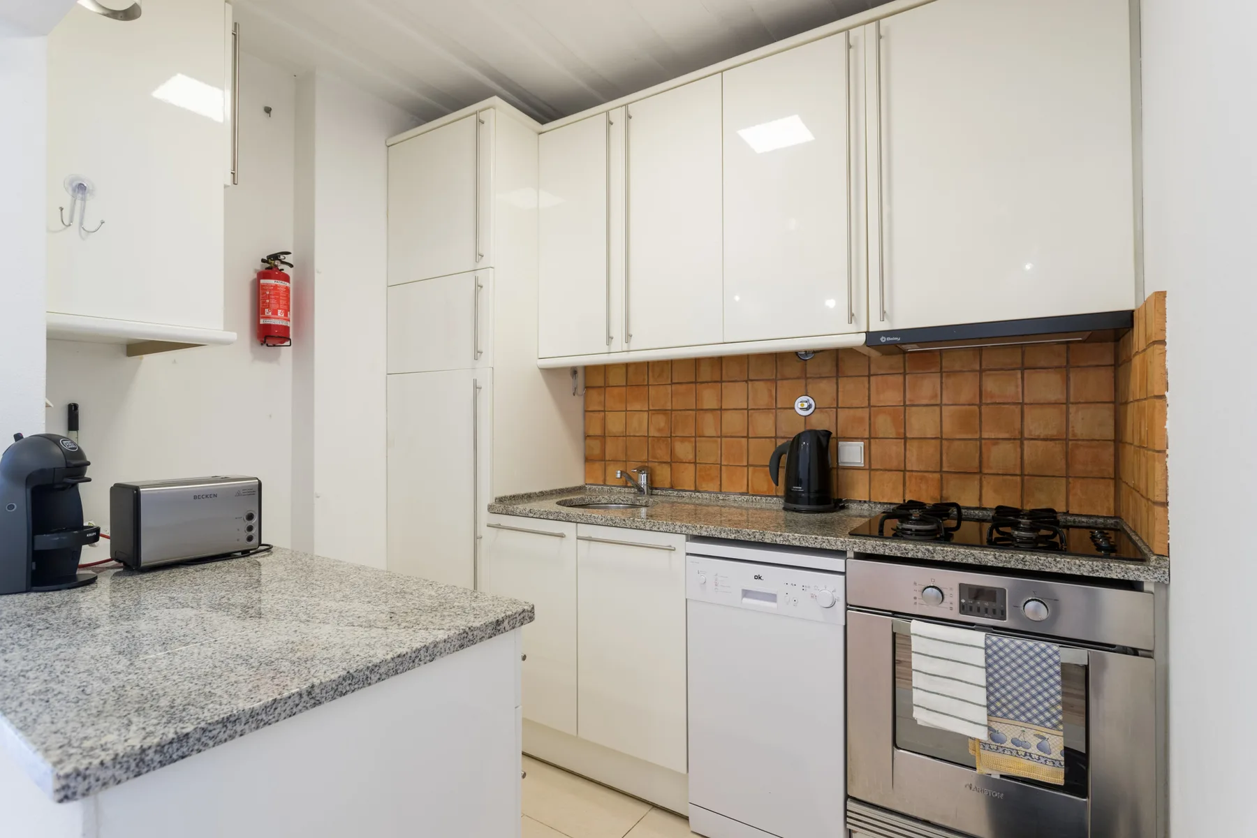 Una cocina luminosa con armarios blancos, una encimera y electrodomésticos.