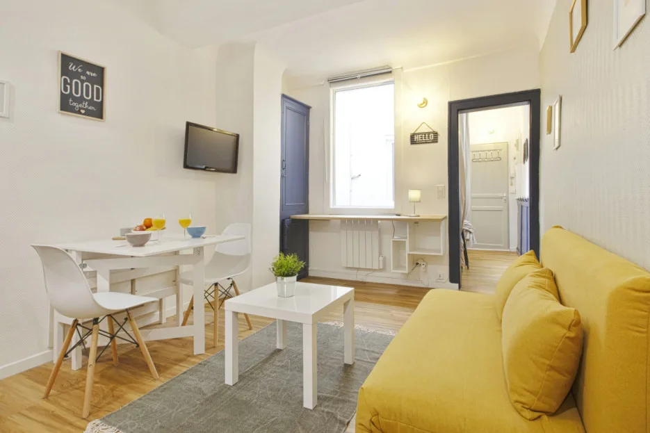 A bright living and dining area with a yellow sofa, table, and large window.