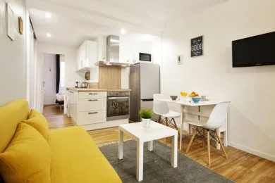 A bright living and dining area has yellow seating beside a compact kitchen.