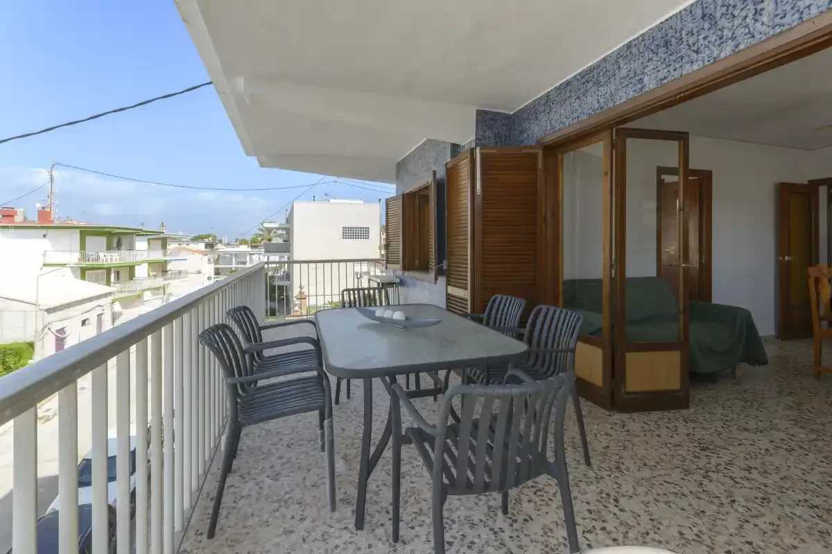 A covered balcony with a dining table and chairs overlooks nearby buildings.