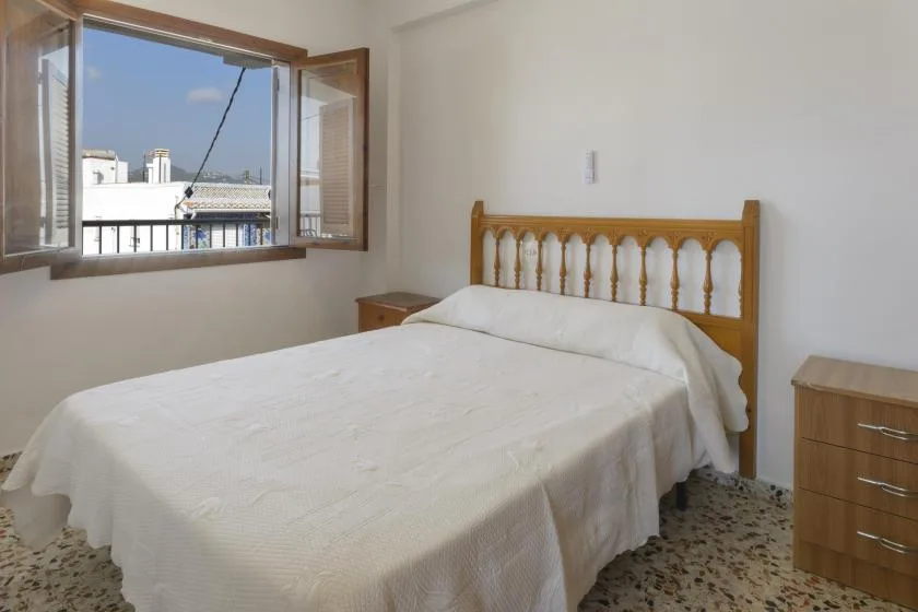 A bedroom with a bed beside an open window.