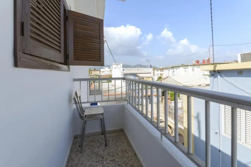A narrow balcony with metal railings and a chair overlooks nearby buildings.