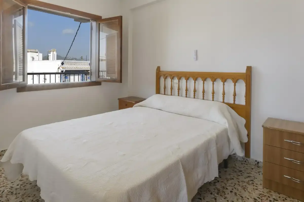 A bedroom with a wooden bed beneath an open window.