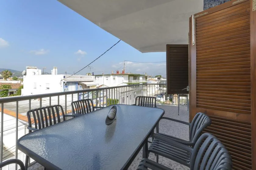 A balcony dining area with a table, seating, and views of nearby buildings.
