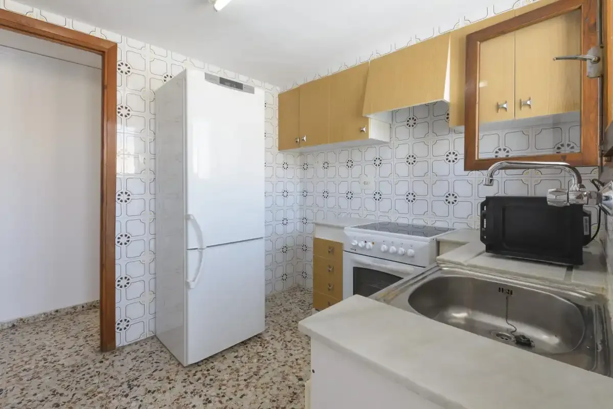 A kitchen with a refrigerator, cabinets, stove, and sink.