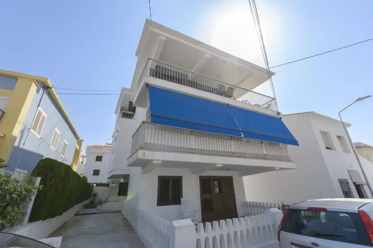 A white multi-story building with blue awnings stands beside a narrow driveway.