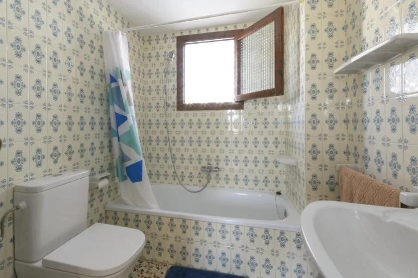 A tiled bathroom with a bathtub, shower curtain, and open window.