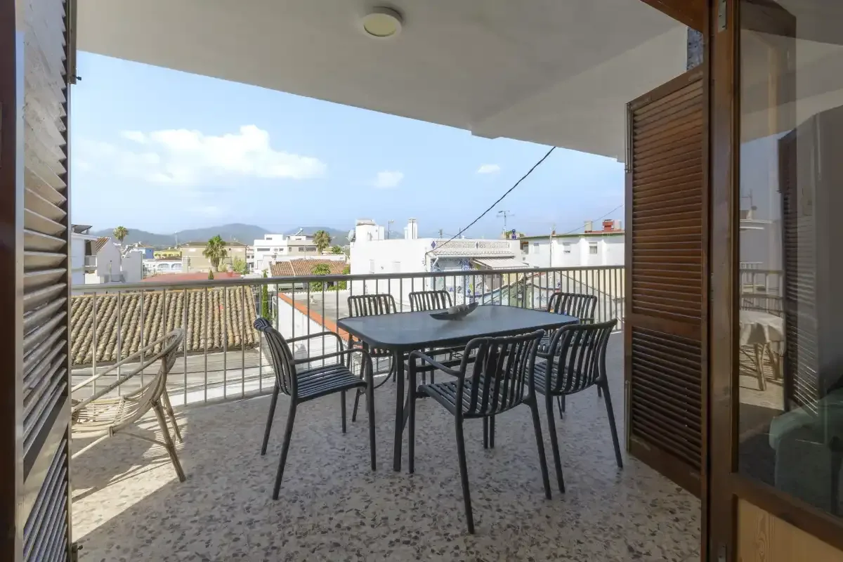 A covered terrace with a dining table and chairs overlooks nearby rooftops.