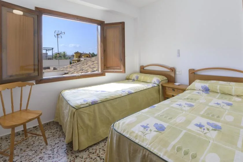 A bedroom with two beds beside an open window.