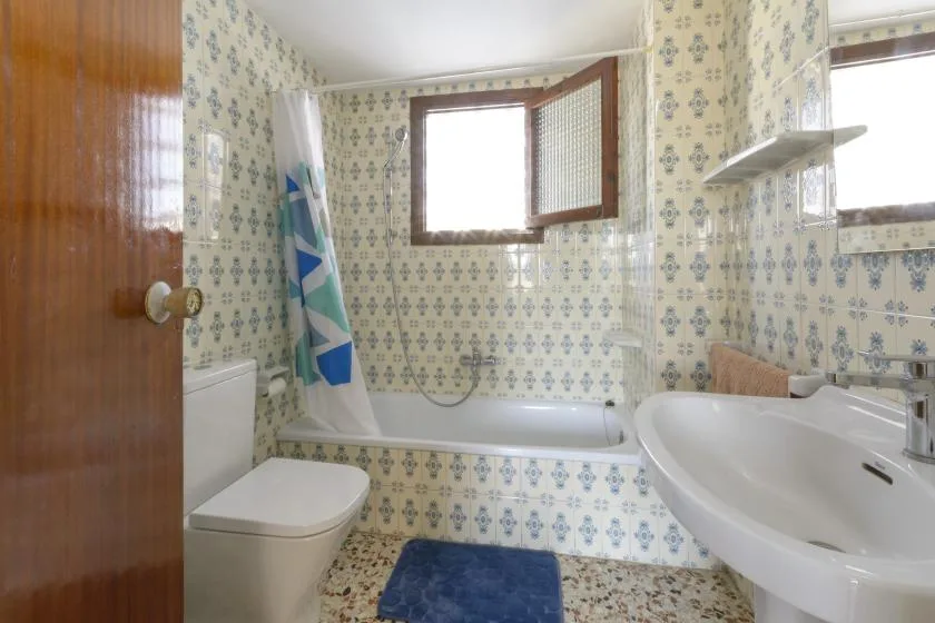 A tiled bathroom with a bathtub, shower curtain, toilet, and sink.