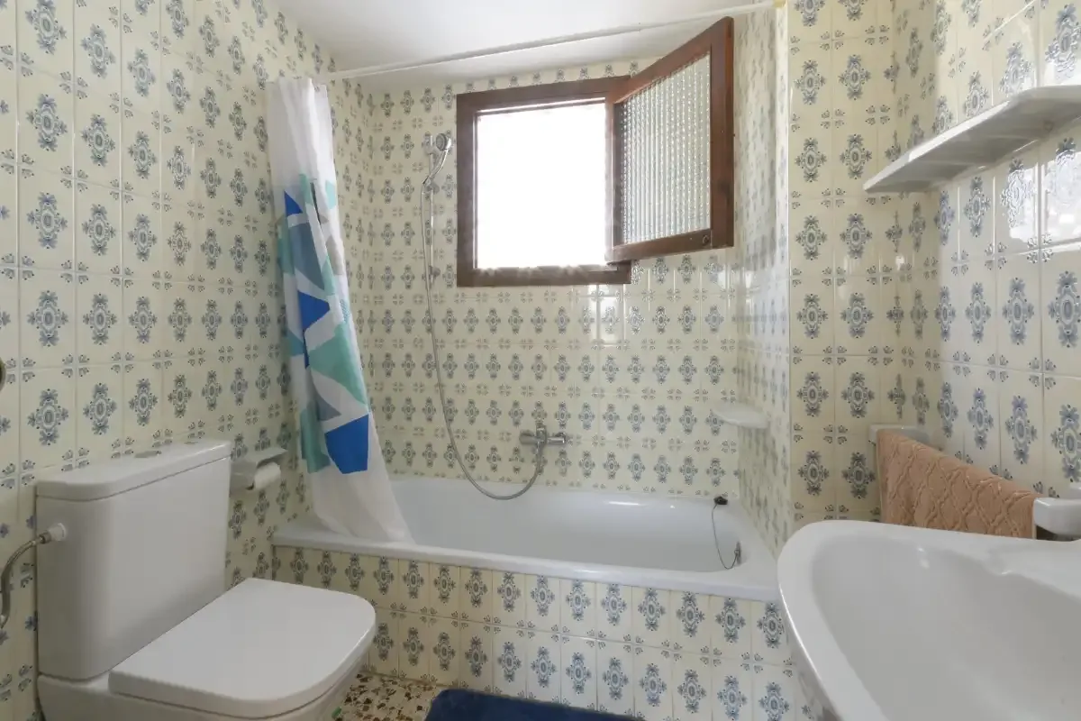A tiled bathroom with a bathtub, shower, toilet, and open window.