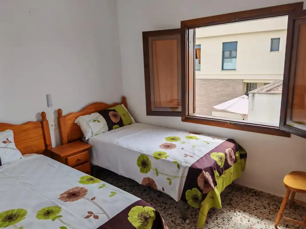 A bedroom with two beds covered in floral-patterned bedding beside an open window.
