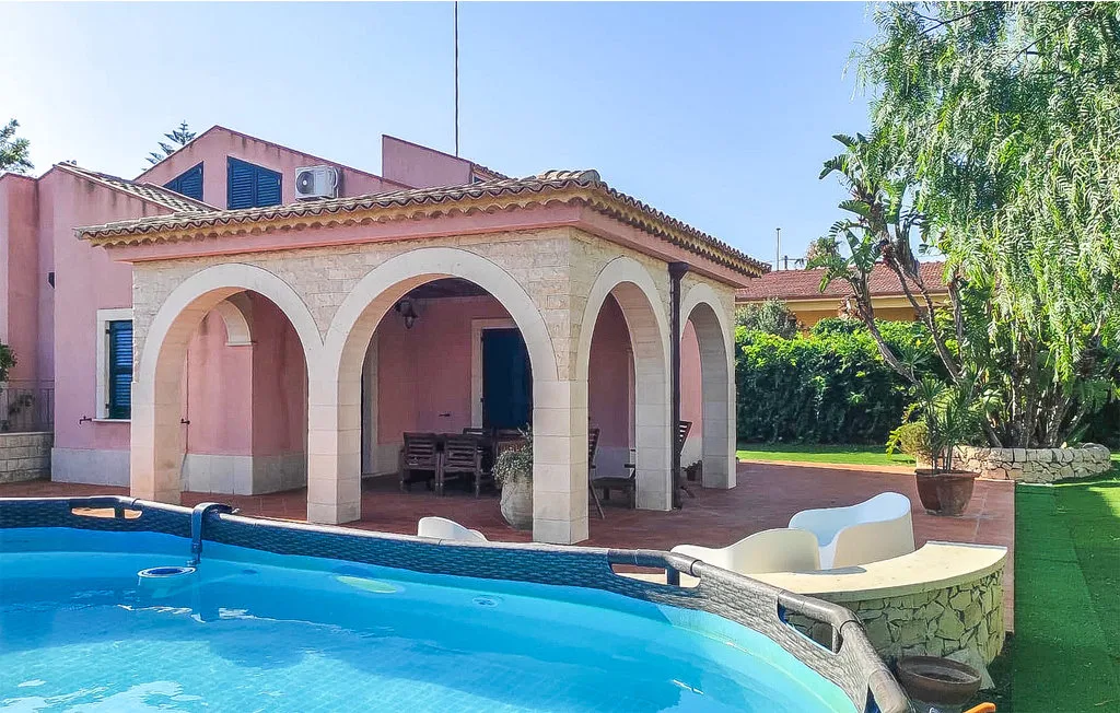 A swimming pool beside a pink building with an arched covered patio.