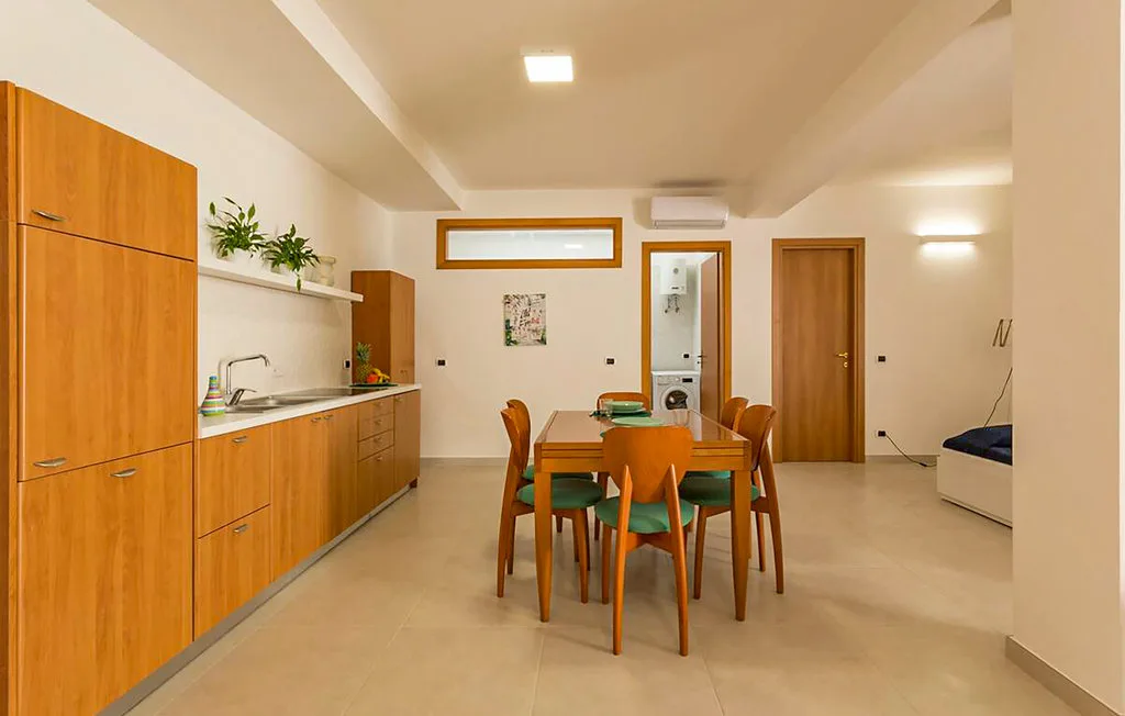 A dining area with a wooden table and chairs beside a kitchenette.