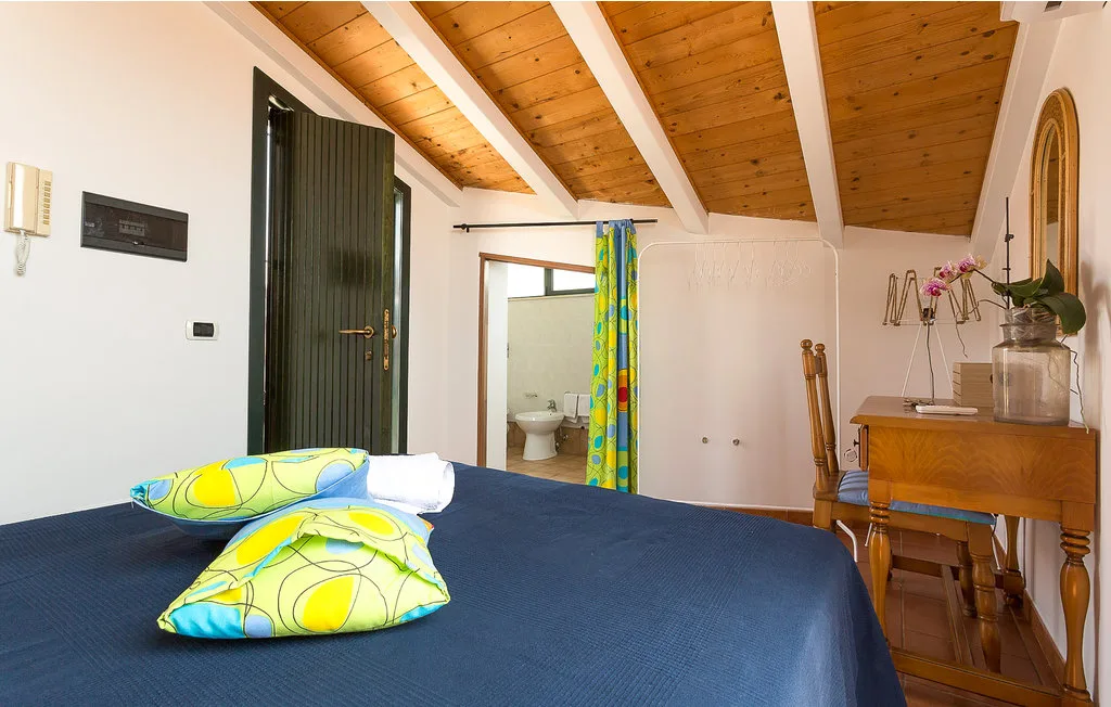 A bedroom with a bed, wooden ceiling, and an open bathroom doorway.