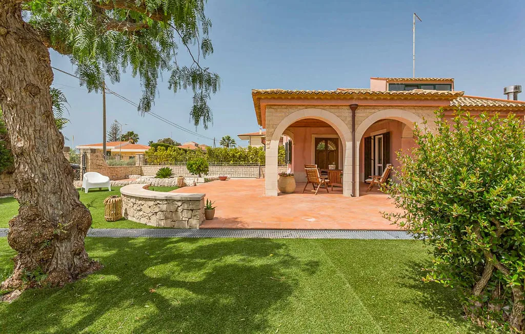 A landscaped garden with a tiled patio and arched house facade.