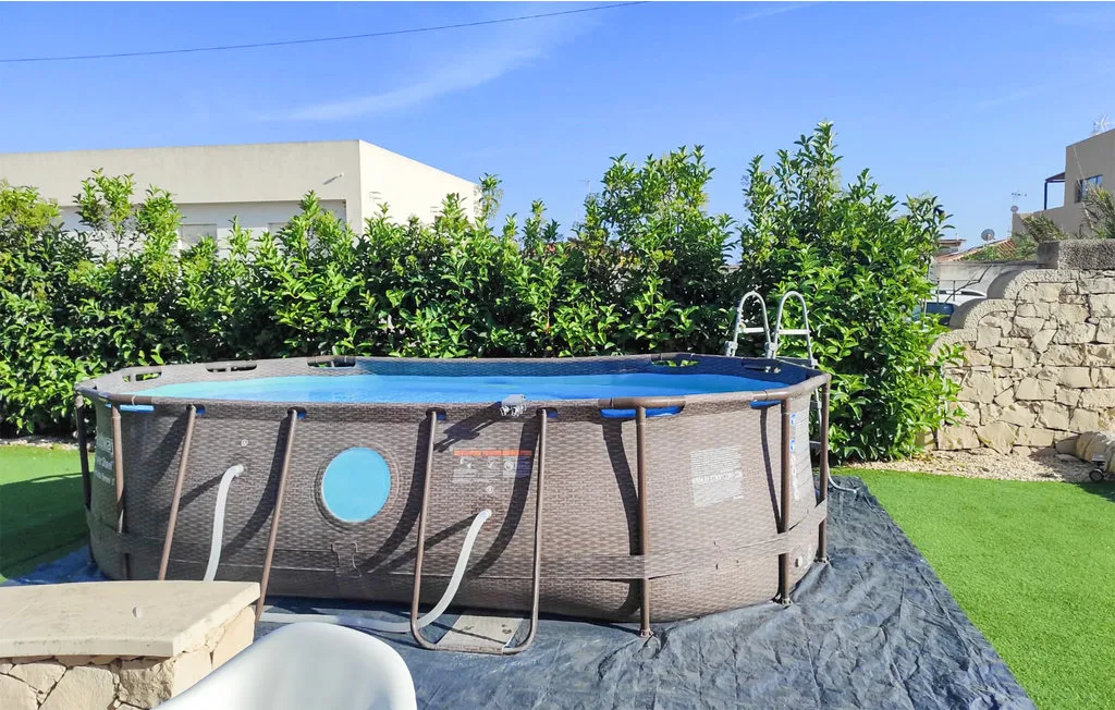 An above-ground pool sits on a paved patio beside a green lawn.