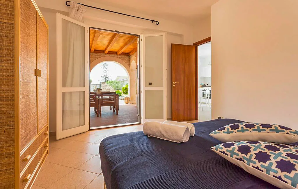A bedroom with a bed facing open doors to a covered dining patio.