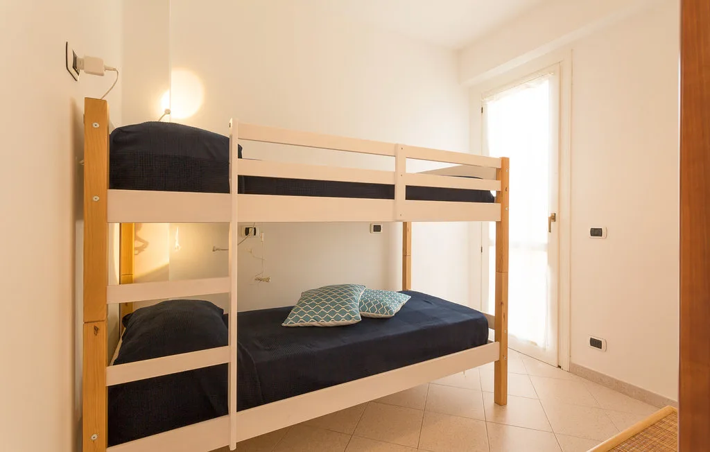A bedroom with a wooden bunk bed and dark bedding beside a bright window.