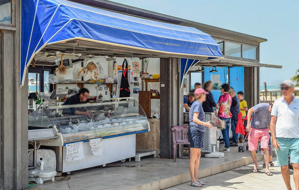 An open seafood counter sits beneath a blue awning as customers gather outside.