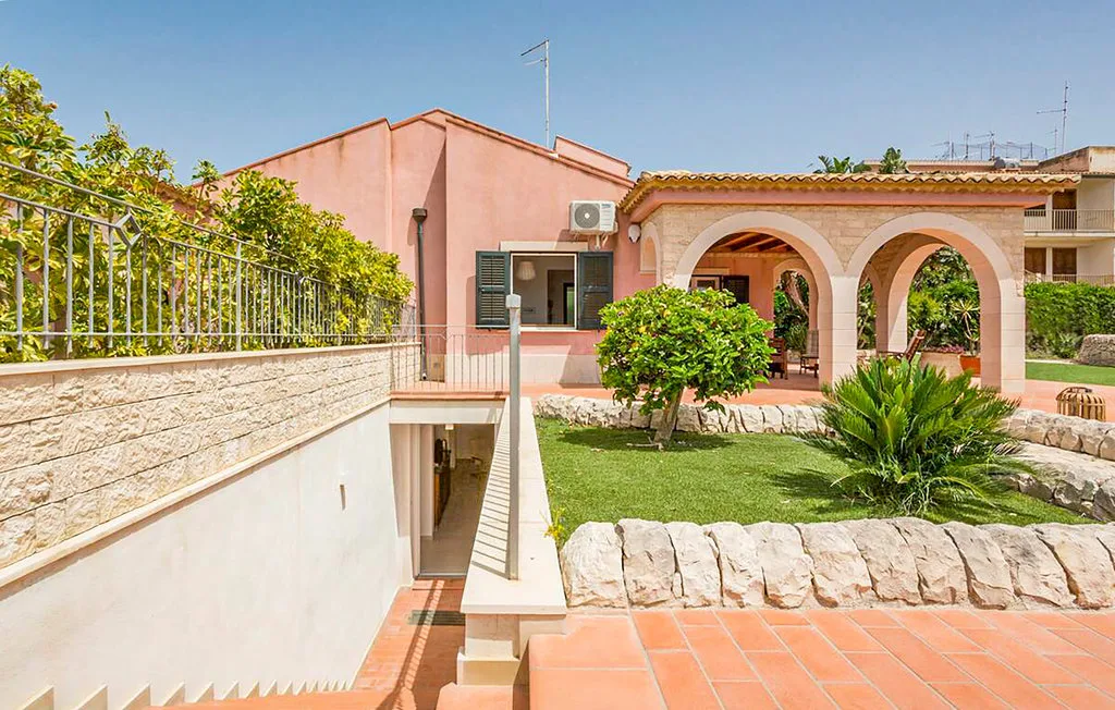 A pink building and arched patio overlook a landscaped garden and tiled terrace.