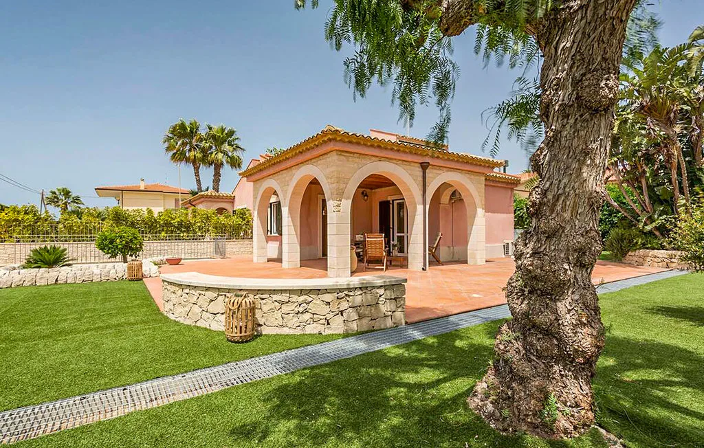 A pink stucco patio with arched openings, outdoor seating, and a stone basin.