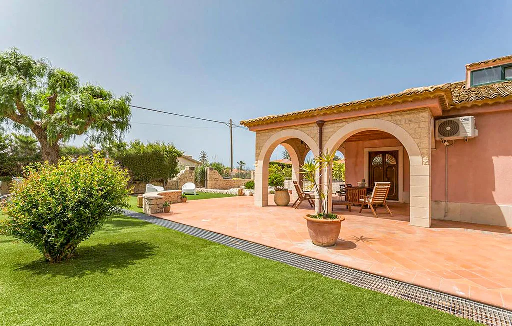 A tiled patio with arched openings overlooks a green lawn.