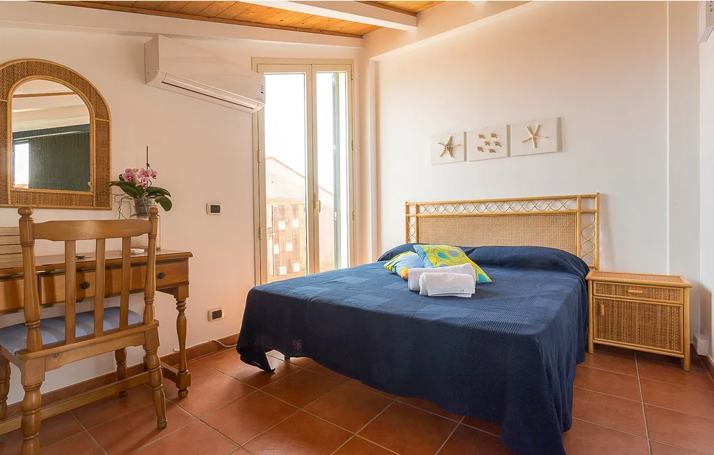 A bedroom with a bed, wooden desk, and a glass door opening to a balcony.