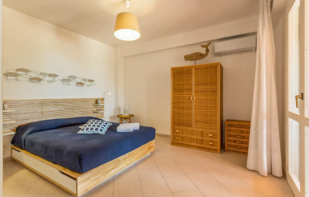 A bedroom with a bed, wooden wardrobe, and curtains beside a window.